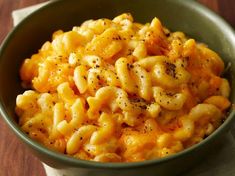 a green bowl filled with macaroni and cheese on top of a wooden table