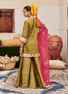 A captivating combination, this green raw silk sharara set features exquisite mirror work on the tunic, creating a striking focal point. Paired with matching pants and a contrasting pink organza dupatta, this ensemble beautifully balances elegance and vibrancy, making it a perfect choice for festive celebrations and special occasions. Raw Silk Sharara, Pink Organza Dupatta, Silk Sharara, Beach Wedding Guests, Jacket Cape, Ritu Kumar, Sharara Set, Organza Dupatta, Matching Pants