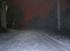 a blurry photo of a road at night with snow on the ground and trees in the background