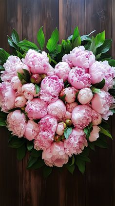 a bouquet of pink peonies with green leaves on a wooden background in the shape of a heart