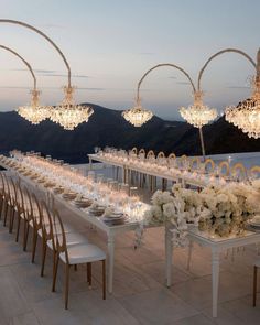 a long table is set with white flowers and crystal chandeliers for an elegant dinner