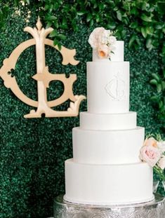 a white wedding cake sitting on top of a table next to a wooden monogram