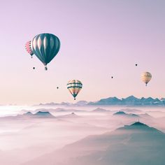 several hot air balloons flying in the sky above some mountains and valleys with fog on them