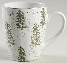 a white coffee cup with trees painted on it's side and gold sprinkles