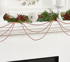 a white mantle decorated with greenery and red berries