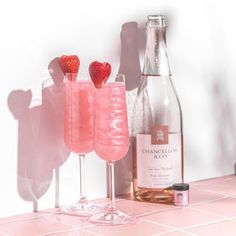 two wine glasses filled with pink liquid and strawberries next to a bottle of champagne