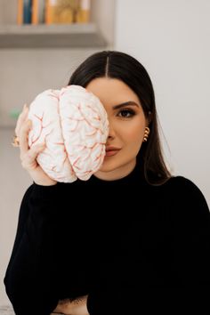 a woman holding up a brain model in front of her face and looking at the camera