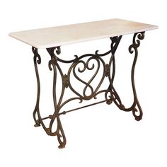 a white marble top table with wrought iron legs and an intricately shaped design on the base