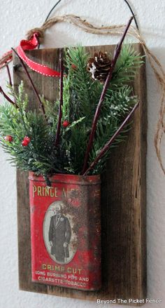 an old tin can with pine branches in it is hung on a wooden wall ornament