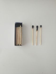 several matches are in a black box on a white surface next to two sticks and an empty container