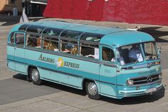 an old blue bus is parked on the side of the road in front of a red building