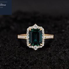 an emerald and diamond ring on top of a black surface