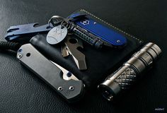 several different types of knifes and keys on a black leather case with blue accents