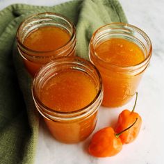 three jars filled with orange colored liquid next to two cherries