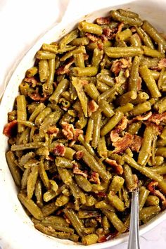 a white bowl filled with green beans and bacon on top of a table next to a spoon