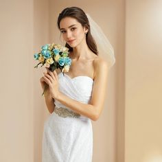 a woman in a white wedding dress holding a bouquet of blue and yellow flowers with a veil on her head