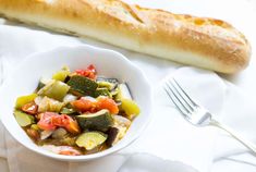 a white bowl filled with vegetables next to a baguette on top of a table