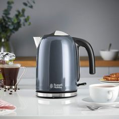 an electric kettle sitting on top of a counter next to coffee cups and saucers