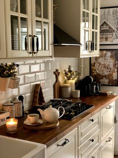 a kitchen with white cabinets and wooden counter tops, candles on the stove top and pictures hanging above it