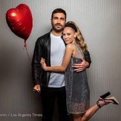 a man and woman standing next to each other in front of a wall with a heart balloon