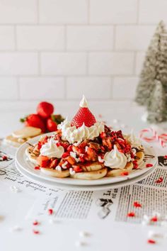 a white plate topped with pancakes covered in whipped cream and strawberries next to a christmas tree