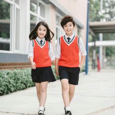 two children in school uniforms are walking down the sidewalk