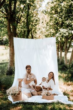 a man, woman and child sitting on a blanket in the grass under some trees