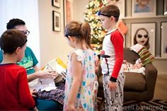 three children standing in front of a christmas tree with presents on the floor and two adults looking at them