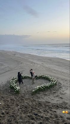 two people standing in the sand with a heart made out of flowers