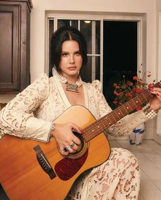 a woman sitting in a kitchen holding an acoustic guitar