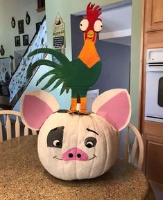 a pumpkin decorated with an animal head and a rooster on it's back sitting on a kitchen table