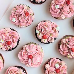 cupcakes with pink frosting and strawberries are arranged on a white surface