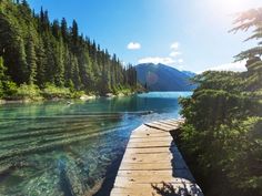 a wooden dock sitting on the side of a lake surrounded by trees and water with mountains in the background