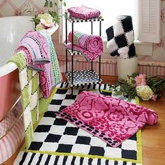 a bath tub sitting next to a window filled with pink and green towels on top of a wooden floor