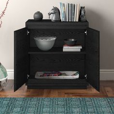 a black cabinet sitting on top of a wooden floor next to a vase and bookshelf