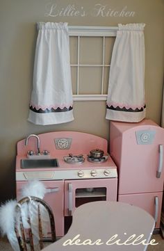 an old fashioned pink kitchen with white curtains and window valance, in a child's playroom