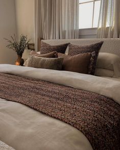 a large bed with pillows and blankets in a bedroom next to a window filled with curtains