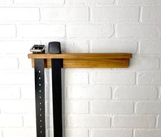 a wooden shelf with a cell phone on it next to a black belt and white brick wall