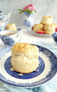 biscuits on a blue and white plate next to teacups with flowers in the background