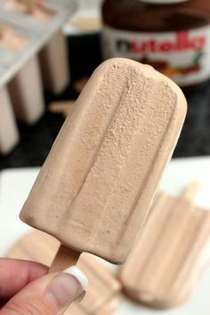 a hand holding a popsicle with peanut butter on it and other ingredients in the background