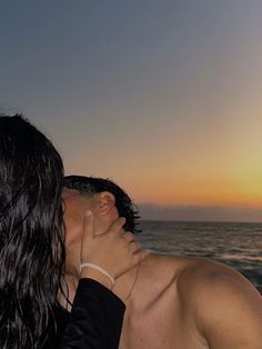 a man and woman kissing in front of the ocean at sunset or sunrise with their faces close to each other