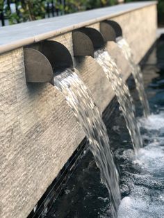 water gushing out from the side of a wall into a pool with fountains in it