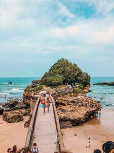 people are walking on the boardwalk near the water and rocks at the beach with an island in the background