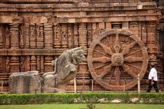 a man walking past an elaborately carved stone structure with a large wheel on it's side