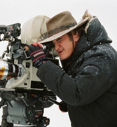 a man with a hat on holding a camera in front of a snow covered field