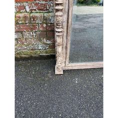 an old mirror sitting on the ground next to a brick wall