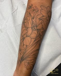 Shows a black linework tattoo of Daffodils and daisies with shading on a forearm Daffodil Half Sleeve Tattoo, Large Daffodil Tattoo, Daffodil Line Art Tattoo, Daisy And Daffodil Tattoo, Daffodil Tattoo Black And White, Daffodil Tattoo Shaded, Fine Line Flower Tattoo Sleeve, Daffodil Tattoo Sleeve, Daffodils Tattoo