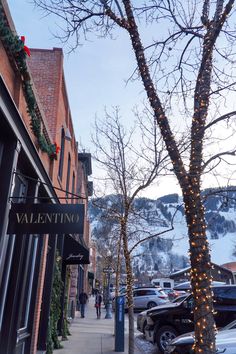 a street with cars parked on the side of it and christmas lights hanging from the trees