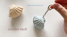 a hand holding a keychain that has two seashells on it and the words crochet shell