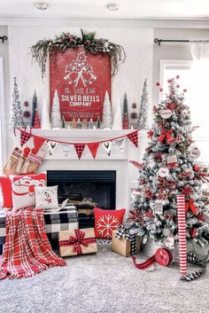 a christmas tree and presents in front of a fireplace with stockings on the mantel